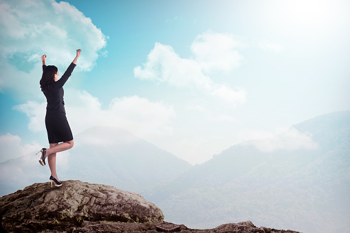Asian business woman standing on the top of the mountain. Business success concept