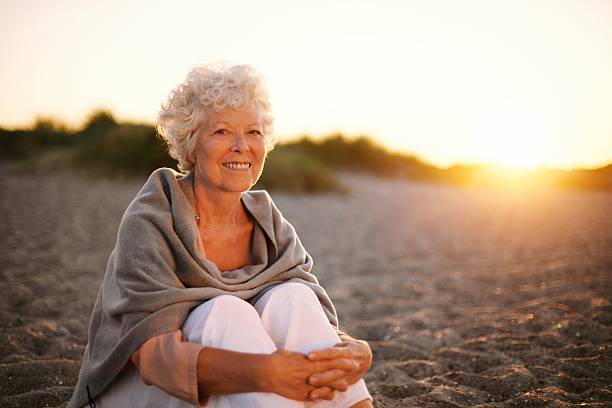 istock Smiling old woman sitting on the beach 486858771
