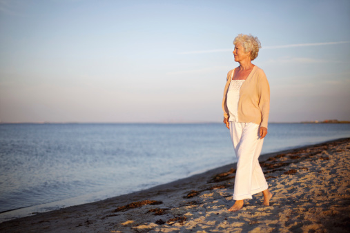 Portrait of a mature woman walking on the beach looking at the sea. Relaxed old lady strolling on the beach with lots of copyspace.