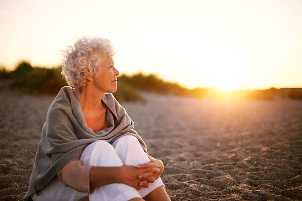 femme d'âge mûr sur la plage regardant vers l'horizon - clothing satisfaction enjoyment day photos et images de collection