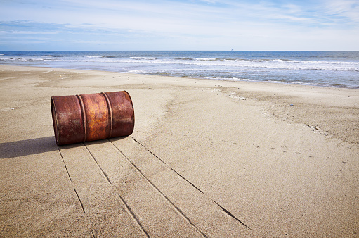 Rusted old barrel on sand beach, coast, sea shore waves, cloudy sky