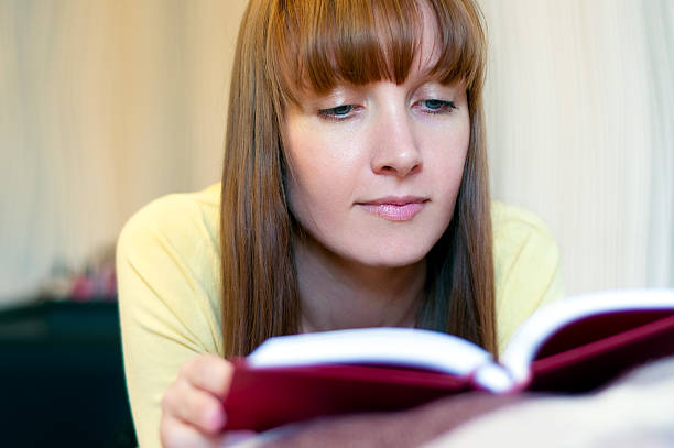 istock Red head woman reading book at home 486860500