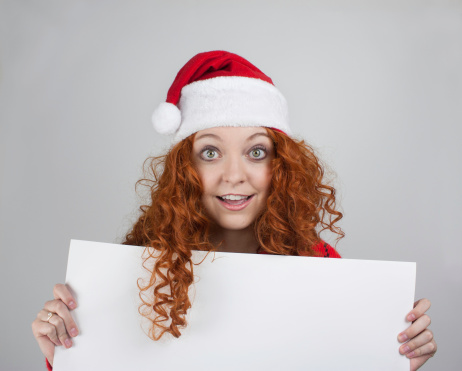 Pretty young woman wearing Santa hat and red sweater holding blank sign