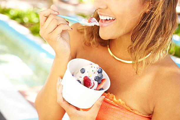 Young African American Woman Enjoying Frozen Yogurt Portrait of a happy young mixed race woman enjoying frozen yogurt with blueberry and strawberry fruit toppings outside. Horizontal shot.file_thumbview_approve.php?size=1&id=20288351 frozen yoghurt stock pictures, royalty-free photos & images