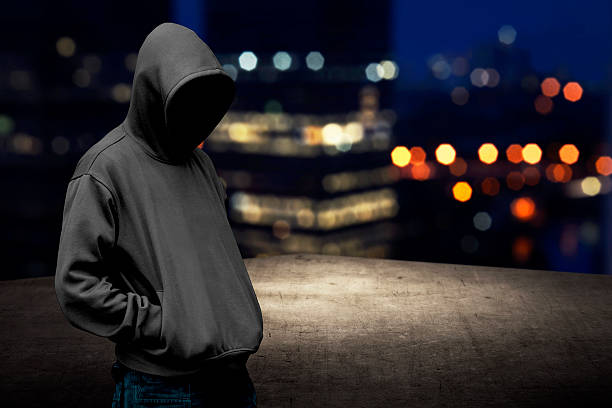 Faceless man in hood on the rooftop Faceless man in hood on the rooftop with city background at night time crime stock pictures, royalty-free photos & images