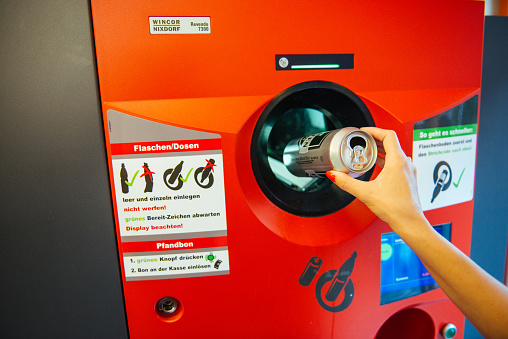 Berlin, Germany - August 31, 2015: Unrecognizable woman throwing empty beer can in recycling machine in order to receive deposit given while paying at the till. In Germany prices are formed on the principle that customar adds 0.08€ when buying drink in glass bottle, while 0.25€ should be added on the beverage price if it is packed in can or plastic bottle. By recycling later on, you receive coupon with that amount which is cashable at the till in any store.