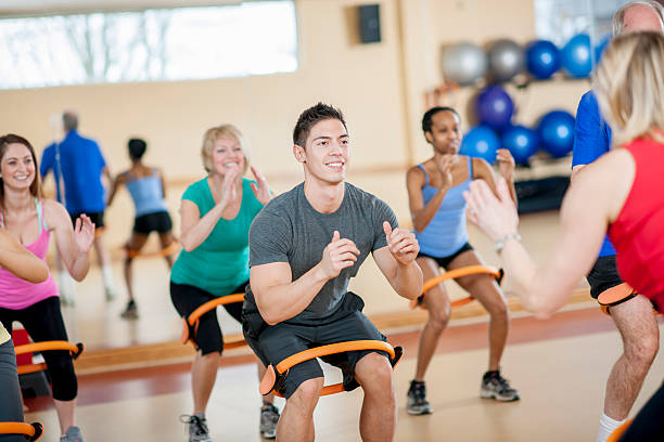 Resistance Band Squats A group of adults are using resistance bands to do arm exercises at a gym fitness class. community health center stock pictures, royalty-free photos & images