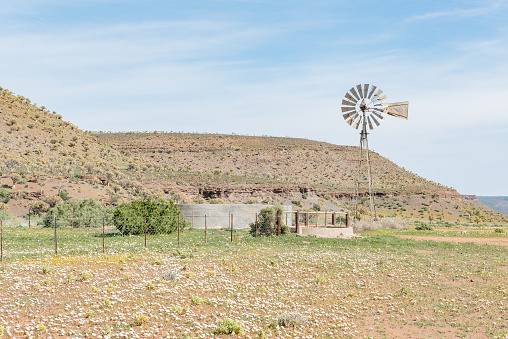 Gannabos, South Africa - August 11, 2015: A water pumping windmill and dam with the Quiver Tree Forest to the left. This area  is usually abundant with wild flowers during August and early September