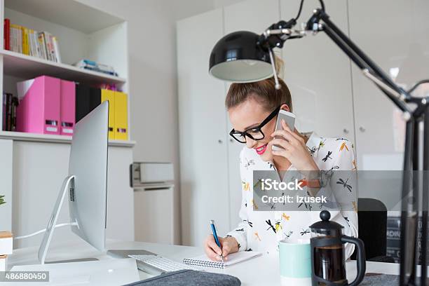 Woman Working In An Office Talking On Smart Phone Stock Photo - Download Image Now - Desk, Graphic Designer, Happiness