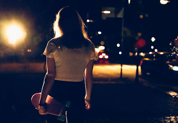 Skater girl walking alone with her skateboard at night
