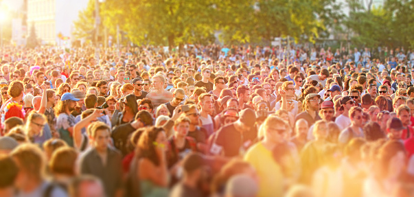 Large crowd of young people crowding city streets in a sunny day during a music festival, walking, dancing and having fun. Street parties are a common way for teenagers to entertain together during the summer in Berlin. Warm sunlight with lens flare. Wideangle horizontal image.