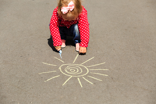little girl drawing sun on asphalt, kids outdoor activities