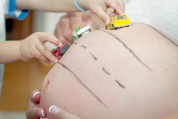 Dad and son playing with toy-cars on mom's belly