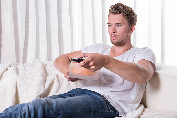istock Portrait young man sitting on couch and eating chips 486896534