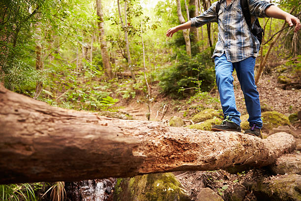 Boy balancing on fallen tree to cross stream in forest