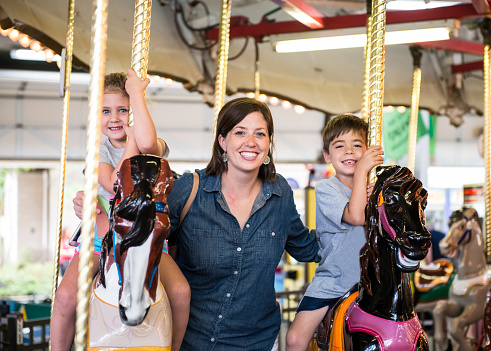 Mother standing between her four year old daughter and six year old son on a carousel in the Funland amusement park in Rehoboth Beach Delaware. It is a popular place for parents to take young children. It has many rides aimed at the youngsters.