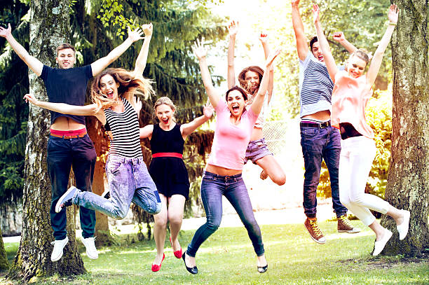 gruppo di amici saltando nel parco - arms raised green jumping hand raised foto e immagini stock