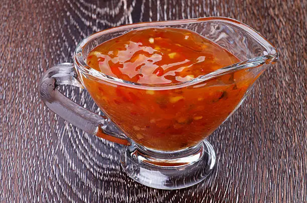 Sweet and Sour Sauce in Glass Gravy Boat isolated on Wooden background