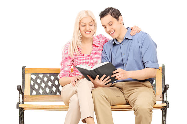 Young couple reading a book seated on bench isolated on white background