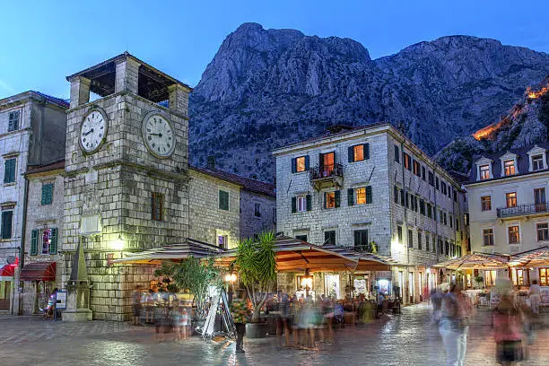 Scene in the medieval town of Kotor, Montenegro at twilight, featuring the Square of Arm and the clock tower near the Maritime entrance gate.