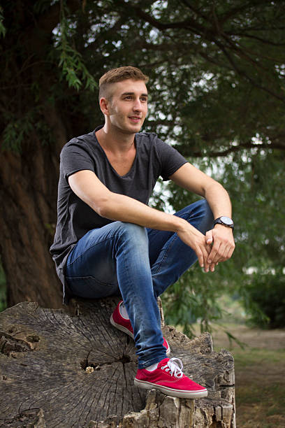 istock Young blond hipster man sitting on wood log. 486922624