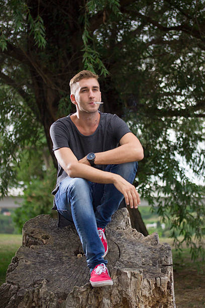 istock Young blond hipster man sitting on wood log. 486925380