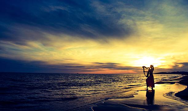 Two friends or couple sitting and talking at sunrise on the beach with the sun in the middle