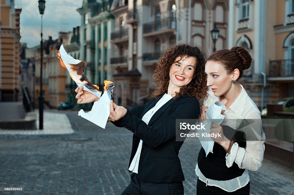 Girl burns the papers a watching other girl. Girl burns the papers a watching the other girl. They are on the streets in the city. 2015 Stock Photo