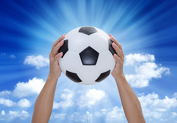 istock Soccer ball in hands with blue sky and lightray background 486936075
