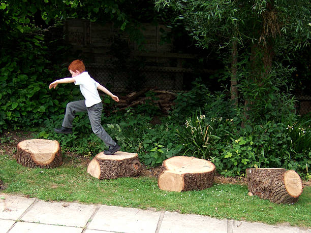 Happy little girl jumping across tree stumps on the playground on an autumn day