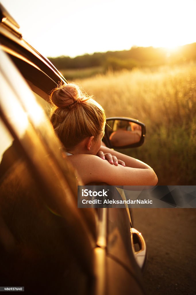 Getaway from the city Young woman looking out of the window of her car and enjoys the view at sunset, getting away from the city  Car Stock Photo