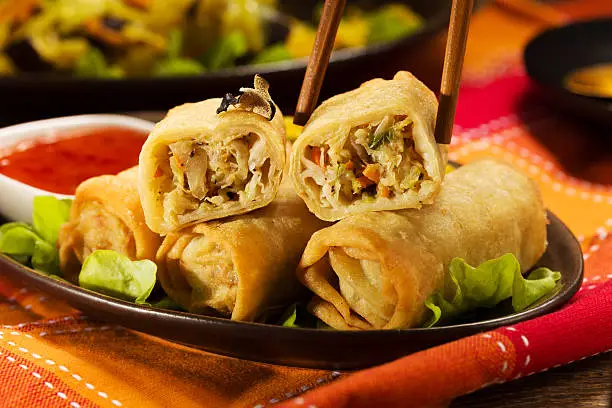 Portion baked spring rolls with vegetables and rice on a plate, served with sauce.