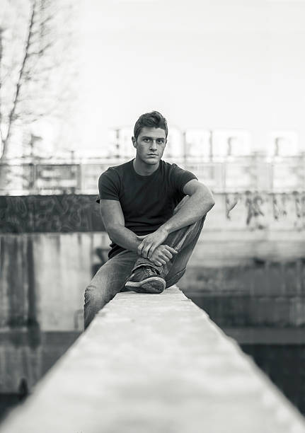 istock Young man sitting on dirty wall, looking at camera 486955814