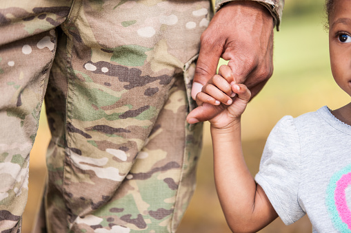 Closeup of a young black girl holding on to her military father's finger with love and trust in him to protect her.