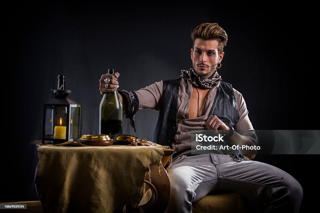 Good Looking Young Man in Pirate Fashion Outfit Sitting next Good Looking Young Man in Pirate Fashion Outfit Sitting next to Table with Candle Lamp, Compass, Gold Pirate - Criminal Stock Photo