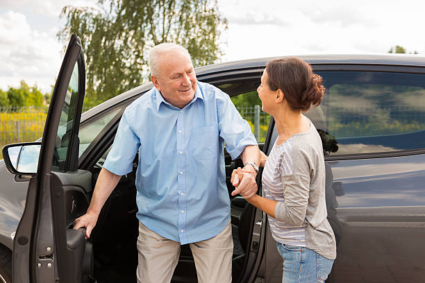 Caregiver helping senior out of the car stock photo