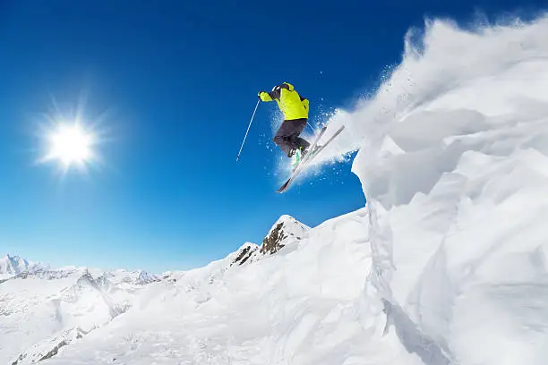 Jumping skier at jump with alpine high mountains
