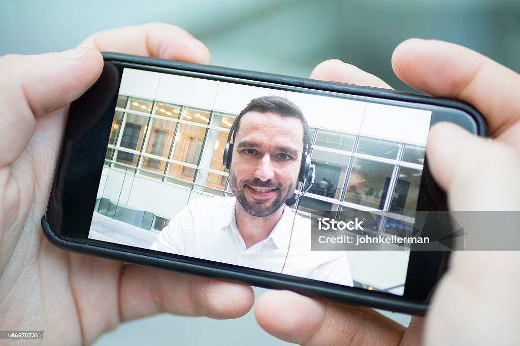 Mano che tiene un uno smartphone durante un skype video - Foto stock royalty-free di Composizione orizzontale