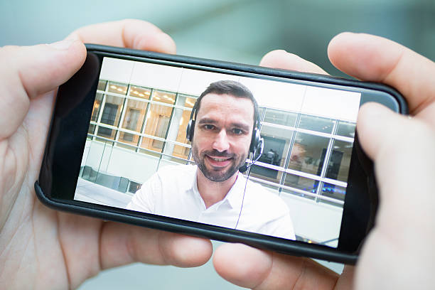 mão segurando um telefone inteligente durante um skype vídeo - skype - fotografias e filmes do acervo