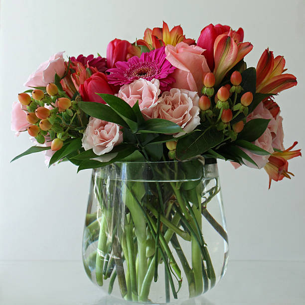 A vase of cut flowers including roses, gerbera daisies, carnations, hypericum berries, alstromeria lilies and tulips.