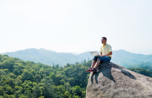 Asian man using laptop on the top of mountain.