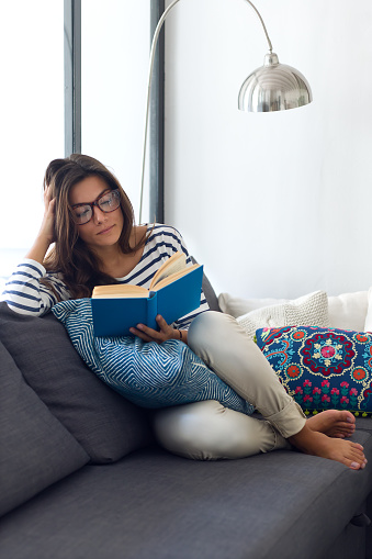 Portrait of beautiful young woman reading a book on the sofa.
