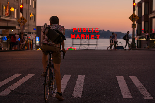 Seattle, USA - August 18, 2015: A man on a bike waiting for the signal to change in front of the famous Pike Place Public Market sign at sunset on Pine street.