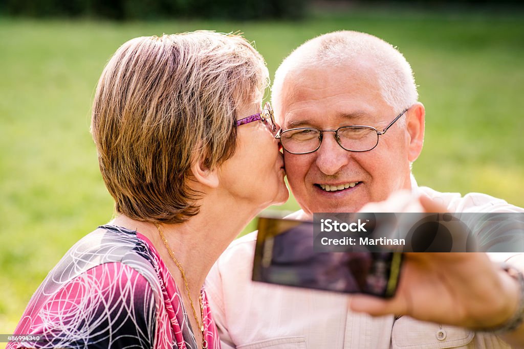 Capturing moments - senior couple Happy senior couple taking picture of themselves by smartphone - woman is kissing man 2015 Stock Photo