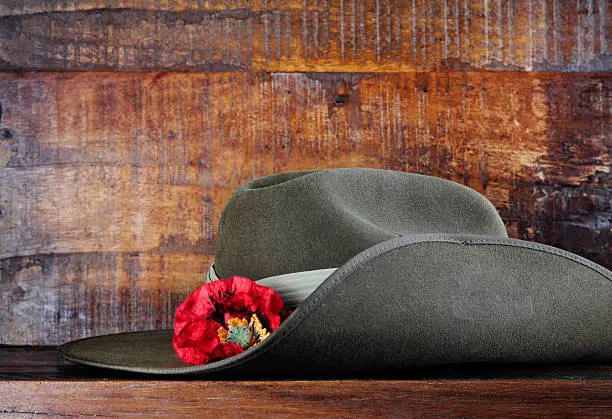 Australian army slouch hat on dark recycled wood with remembrance red poppy for Anzac Day or Remembrance Armistice Day.