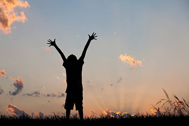 Happy Child in Worship A happy child raising his arms to the sky at sunset. Horizontal colour image. Copyspace. Worship concept. Silhouette. Natural God beams in the sky. religion sunbeam one person children only stock pictures, royalty-free photos & images