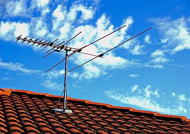 TV antenna on a rooftop with blue sky and white clouds background