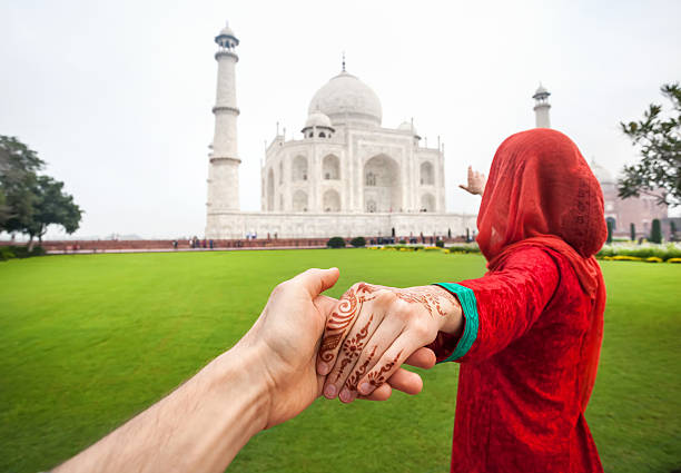 Follow me to Taj Mahal Woman in red Indian costume holding her friend by hand and pointing to Taj Mahal in Agra, Uttar Pradesh, India mausoleum photos stock pictures, royalty-free photos & images