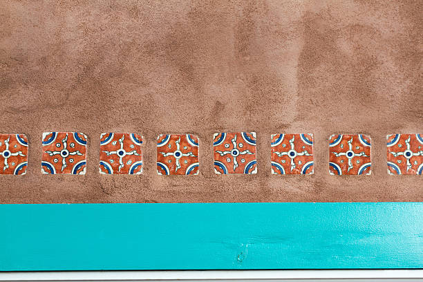 A line of geometric vintage Mexican (Talavera) tiles set into adobe wall above the top of a turquoise window frame. Copy space available.