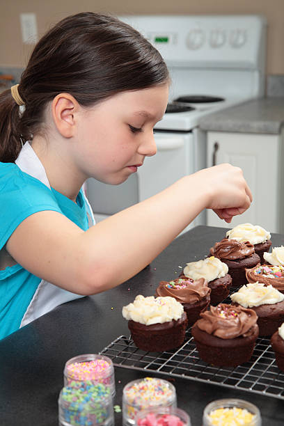 istock Young girl adding sprinkles to cupcakes. 487015299